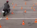 Motocyklista w kasku pokonuje tor przeszkód z pachołków, ćwicząc jazdę na prawo jazdy **kategoria a2**.