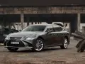 Szary Lexus LS 500h zaparkowany na tle zniszczonej budowli.