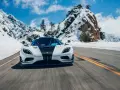 Biały Koenigsegg Agera RS z czarnym pasem na masce pędzi po ośnieżonej górskiej drodze.