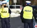 Dwóch policjantów w kamizelkach odblaskowych z napisem "POLICJA" stoi na drodze.