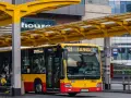 Żółto-czerwony autobus miejski na przystanku. Kierowca autobusu, jak i pasażerowie, zastanawiają się, ile zarabia kierowca autobusu.