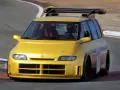 Żółty Renault Espace F1 z kierowcą w kasku na torze wyścigowym. Potężny spojler dachowy i agresywny wygląd.