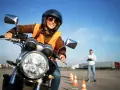 Uśmiechnięta kobieta w kasku i kamizelce na motocyklu, przygotowuje się do egzaminu na prawo jazdy na motor.