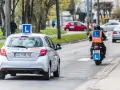 Srebrny samochód z literą "L" na dachu i motocyklista w kamizelce odblaskowej, obaj z literą "L" z tyłu, poruszają się po drodze. To kategoria a nauki jazdy.