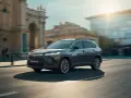 Ciemnoszary Toyota Corolla Cross sunie ulicą miasta, mijając zabytkowe budynki i nowoczesne szklane fasady.
