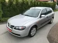 Srebrny Nissan Almera hatchback stoi na asfaltowej drodze, otoczony zielenią.