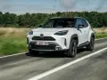 Biały Toyota Yaris Cross jedzie po drodze, otoczony zielenią.