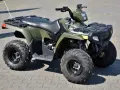 Zielony quad Polaris Sportsman 300 na kostce brukowej.