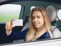 Uśmiechnięta młoda kobieta w samochodzie pokazuje swoje nowe zdjęcie do prawa jazdy.