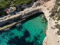 Malta plaże: turkusowa woda w zatoce, skaliste wybrzeże i schody prowadzące do ukrytej plaży. Dwie osoby spacerują po klifie.