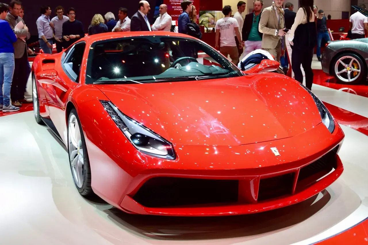 Błyszczące, czerwone Ferrari 488 na wystawie, otoczone przez widzów.
