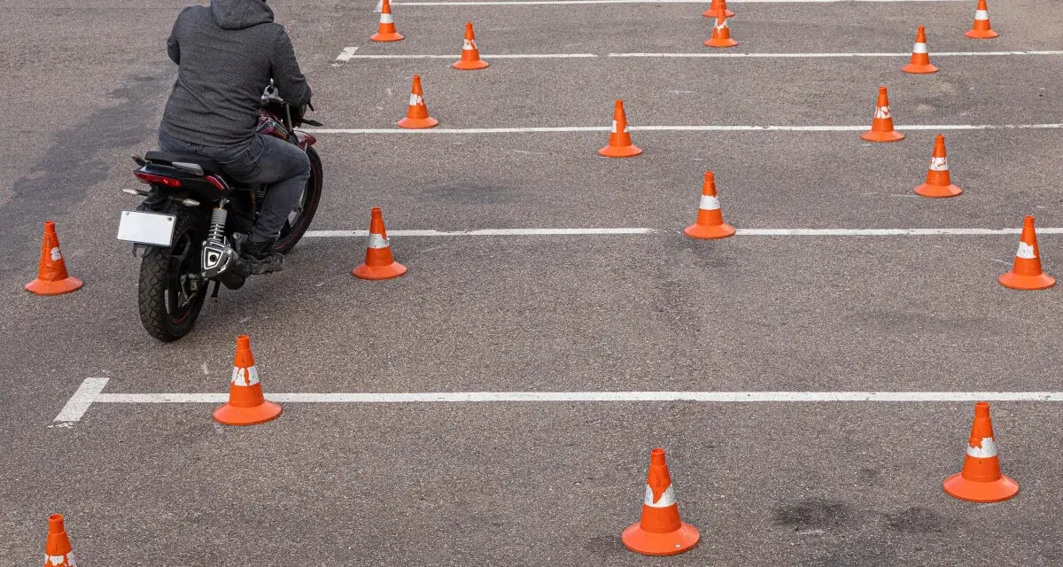 Motocyklista w kasku pokonuje tor przeszkód z pachołków, ćwicząc jazdę na prawo jazdy **kategoria a2**.