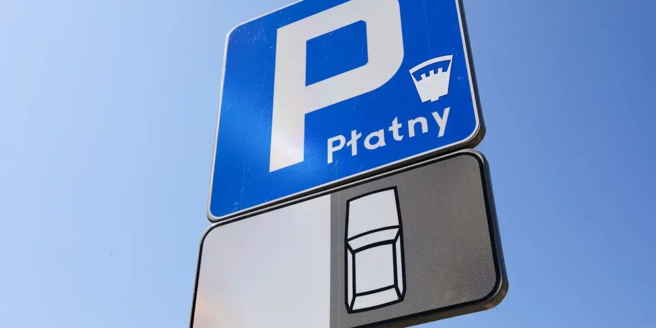 Znak D18 informuje o płatnym parkingu. Widoczny symbol samochodu sugeruje miejsce postojowe.