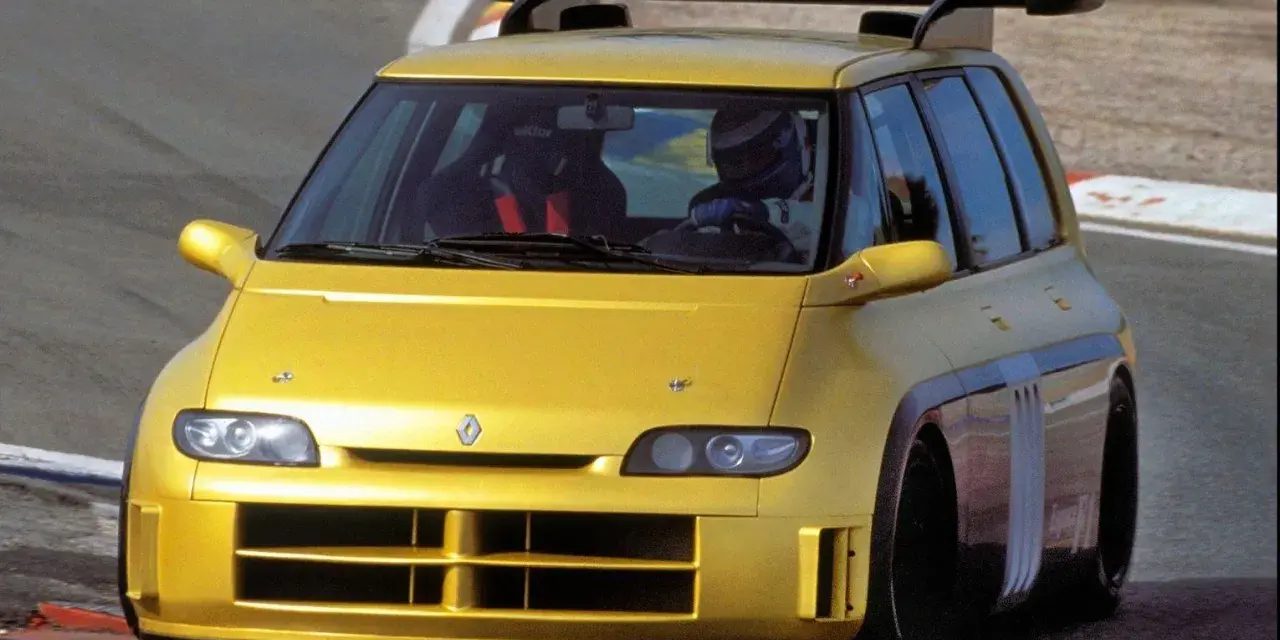Żółty Renault Espace F1 z kierowcą w kasku na torze wyścigowym. Potężny spojler dachowy i agresywny wygląd.