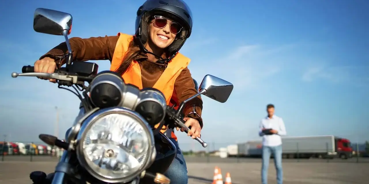 Uśmiechnięta kobieta w kasku i kamizelce na motocyklu, przygotowuje się do egzaminu na prawo jazdy na motor.