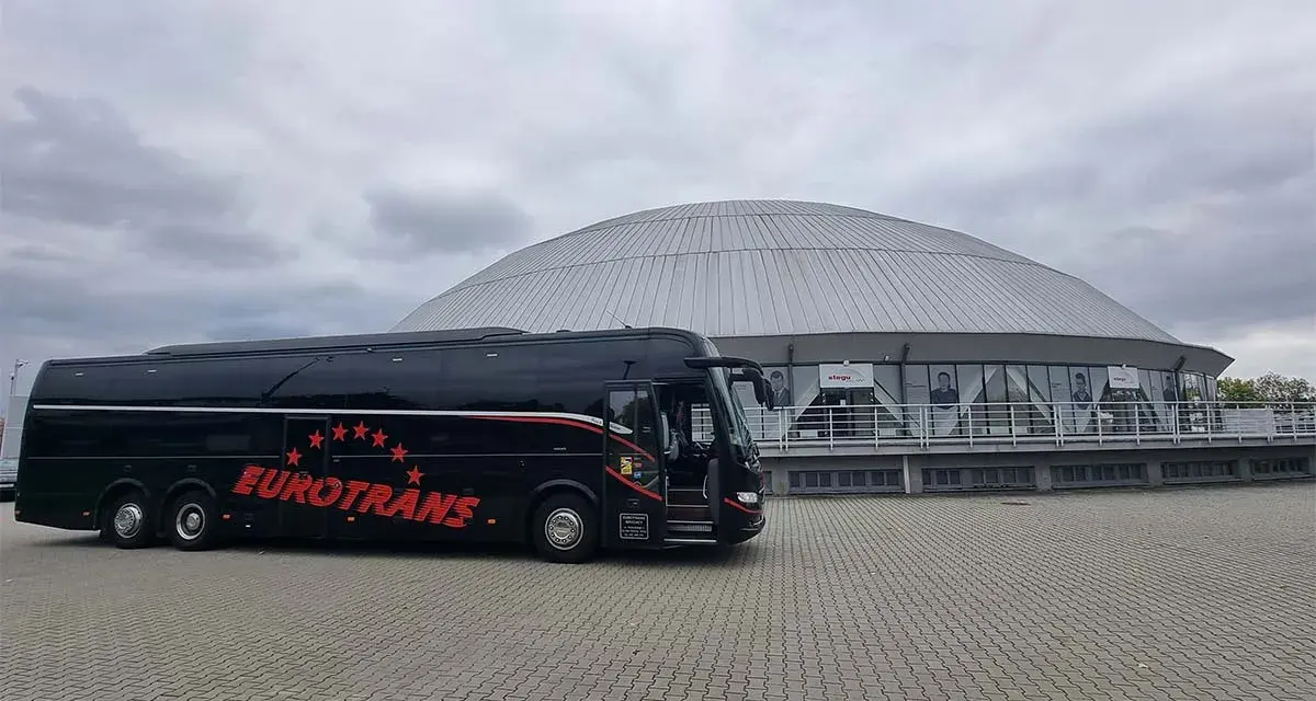 Czarny autokar turystyczny "Eurotrans" przed nowoczesnym budynkiem z kopułą.