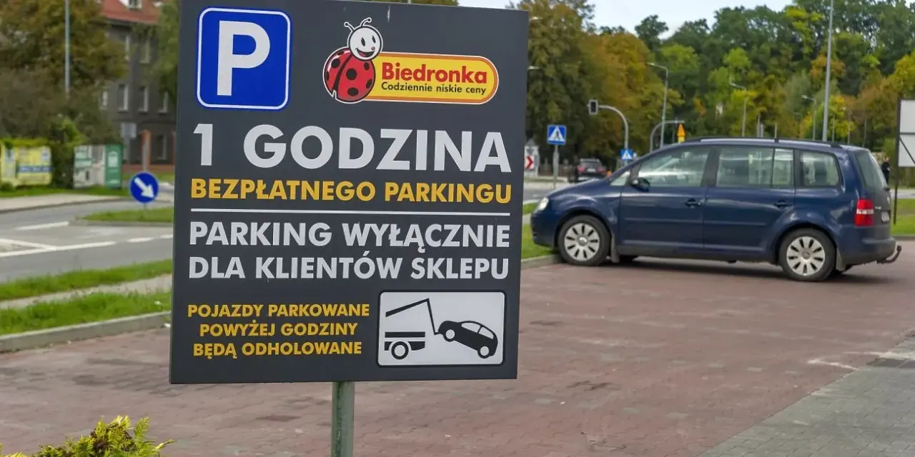 Tablica informuje o 1 godzinie darmowego parkingu dla klientów Biedronki. Pojazdy parkowane dłużej mogą otrzymać mandat za parkowanie i zostać odholowane.