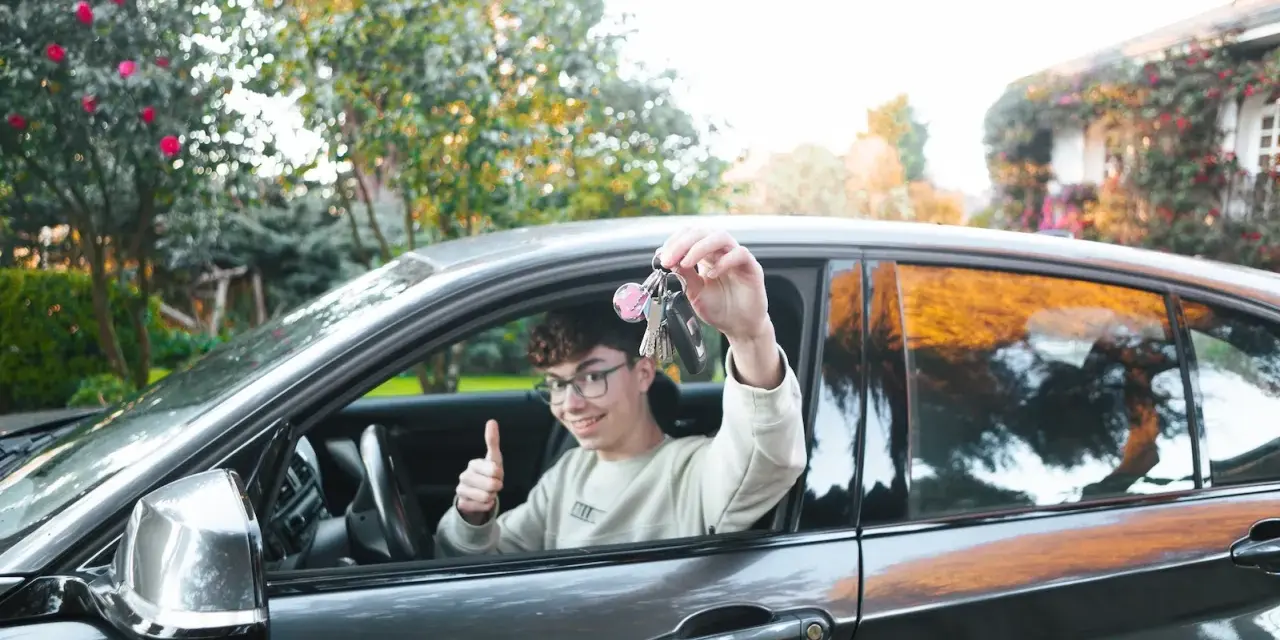 Chłopak z kluczykami w ręku, zadowolony z nowego samochodu. Kategoria B1.