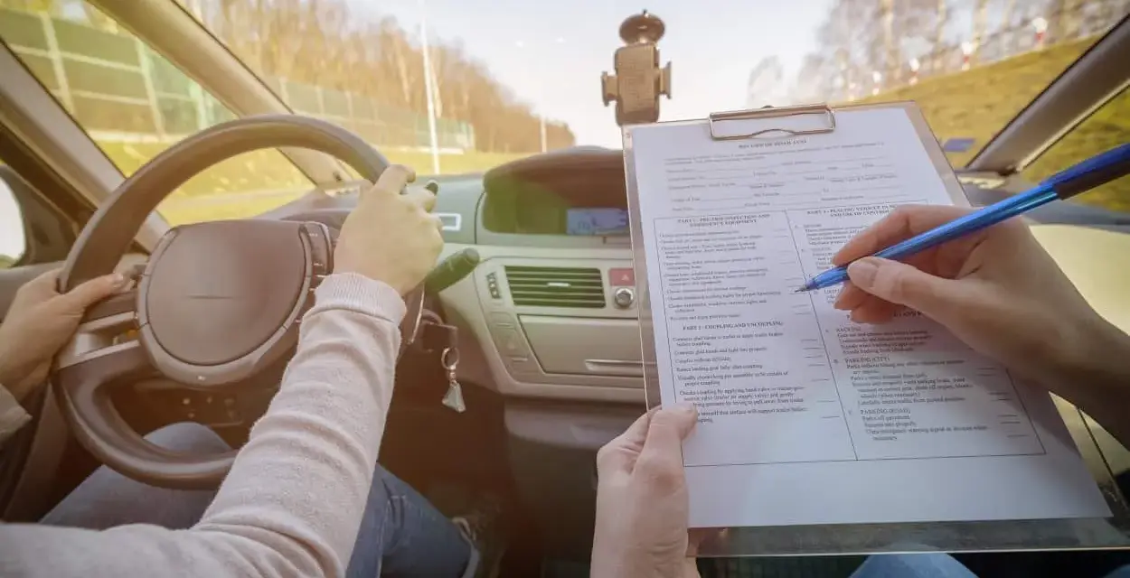 Egzamin na prawo jazdy. Kandydat trzyma kierownicę, a egzaminator zaznacza na liście kontrolnej różne kategorie prawa jazdy.
