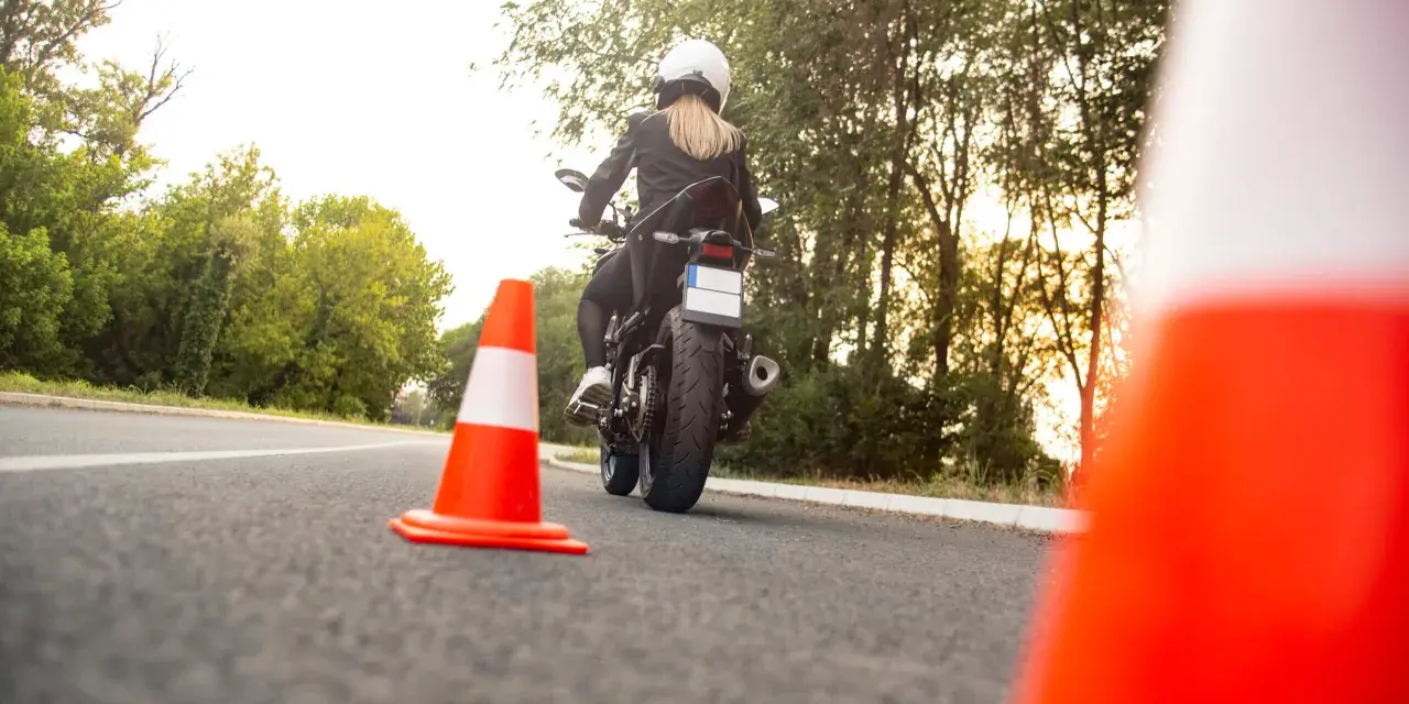Kobieta na motocyklu podczas egzaminu na prawo jazdy kat A. Sprawdza cenę kursu.