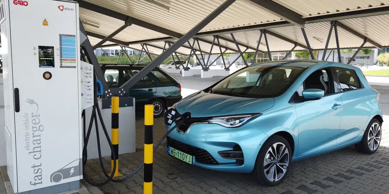 Błękitny Renault Zoe podłączony do ładowarki na parkingu pod zadaszeniem.
