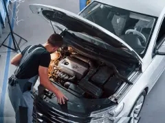 Młody mechanik w kombinezonie pracuje przy silniku białego samochodu. To jego pasja, każdy konstruktor marzy o takiej precyzji.