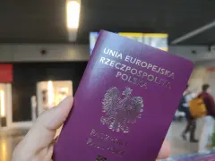 Dłoń trzyma fioletowy paszport Rzeczypospolitej Polskiej z godłem orła.