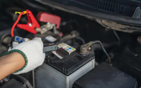 Ręka w białej rękawiczce podłącza kable rozruchowe do akumulatora samochodowego.