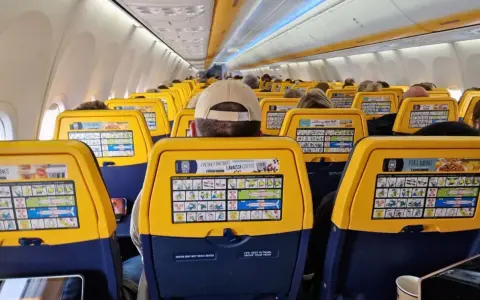 Widok wnętrza samolotu Ryanair z żółtymi oparciami siedzeń i instrukcjami bezpieczeństwa.