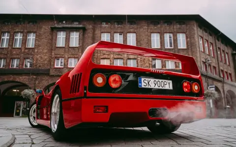 Czerwone Ferrari F40 z dymem z wydechu na tle ceglanego budynku.