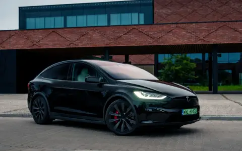Czarny Tesla Model X zaparkowany przed nowoczesnym budynkiem z cegły.