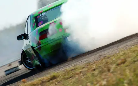 Zielony samochód z kwiatami driftuje, wydzielając dużo dymu.