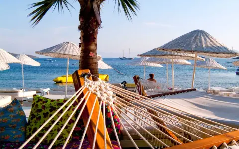 Hamaki i parasole na plaży w Turcji z widokiem na morze i żaglówki.