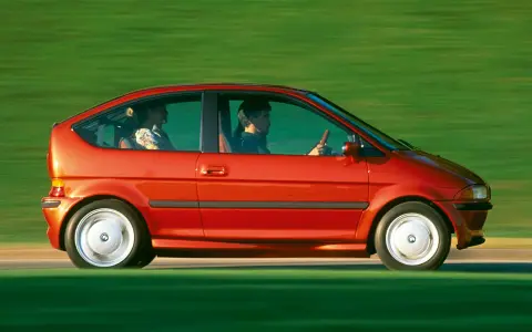 Czerwony samochód elektryczny BMW E1 z lat 90. jadący po zielonym tle.