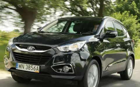 Czarny Hyundai ix35 jedzie drogą wśród zieleni.