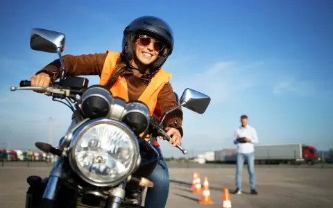 Uśmiechnięta kobieta w kasku i kamizelce na motocyklu, przygotowuje się do egzaminu na prawo jazdy na motor.