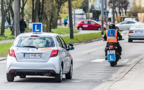 Srebrny samochód z literą "L" na dachu i motocyklista w kamizelce odblaskowej, obaj z literą "L" z tyłu, poruszają się po drodze. To kategoria a nauki jazdy.
