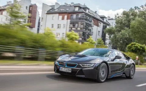 Czarny BMW i8 pędzi ulicą, mijając nowoczesne budynki i zielone drzewa.