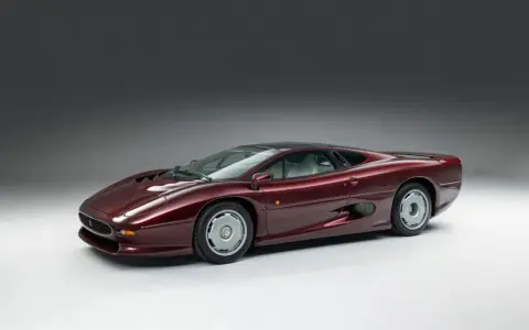 Bordowy Jaguar XJ220, ikona motoryzacji lat 90., prezentuje swoje aerodynamiczne linie na tle szarego tła.
