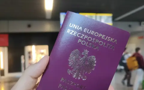 Dłoń trzyma fioletowy paszport Rzeczypospolitej Polskiej z godłem orła.