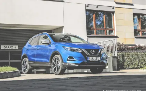 Błękitny Nissan Qashqai 2018 zaparkowany przed nowoczesnym budynkiem z garażem.