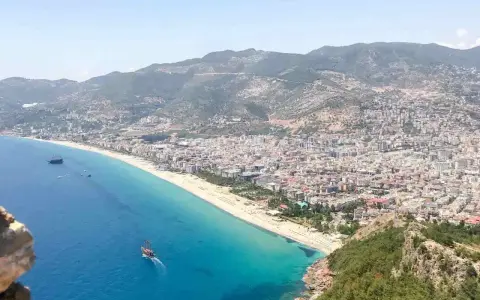 Widok na wybrzeże Turcji z miastem, plażą i statkami na turkusowym morzu.