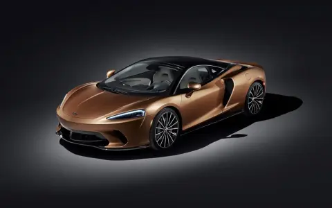 Elegancki, miedziany McLaren GT z czarnym dachem i felgami, prezentujący swoje sportowe linie na ciemnym tle.