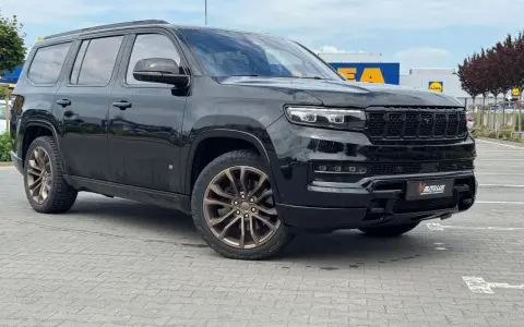 Czarny Grand Wagoneer z brązowymi felgami stoi na parkingu przed sklepami.