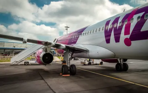 Samolot Wizz Air z fioletowym logo na lotnisku, z drabiną przy skrzydle.