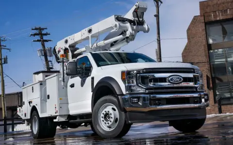 Biały Ford F650 z podnośnikiem koszowym gotowy do pracy przy liniach energetycznych.
