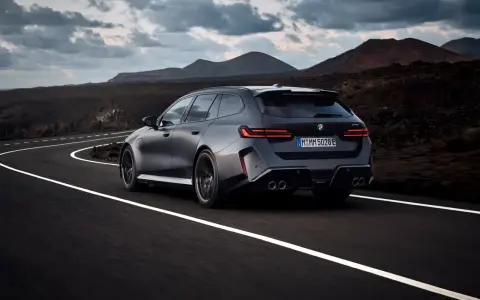 Mocne BMW M5 Touring pędzi po krętej drodze pośród surowego krajobrazu.