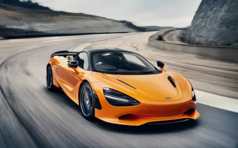 Pomarańczowy McLaren 750S z czarnym dachem sunie po torze wyścigowym, tworząc dynamiczny obraz prędkości i mocy.