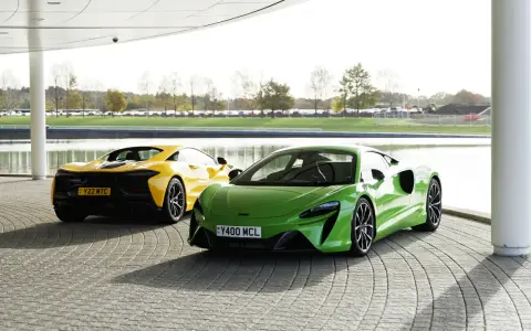 Dwa sportowe samochody McLaren Artura: jeden zielony z przodu, drugi żółty z tyłu, stojące na zewnątrz.