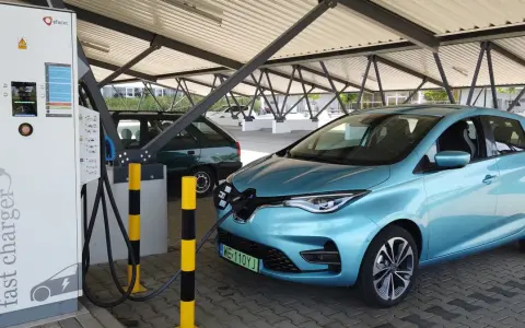Błękitny Renault Zoe podłączony do ładowarki na parkingu pod zadaszeniem.